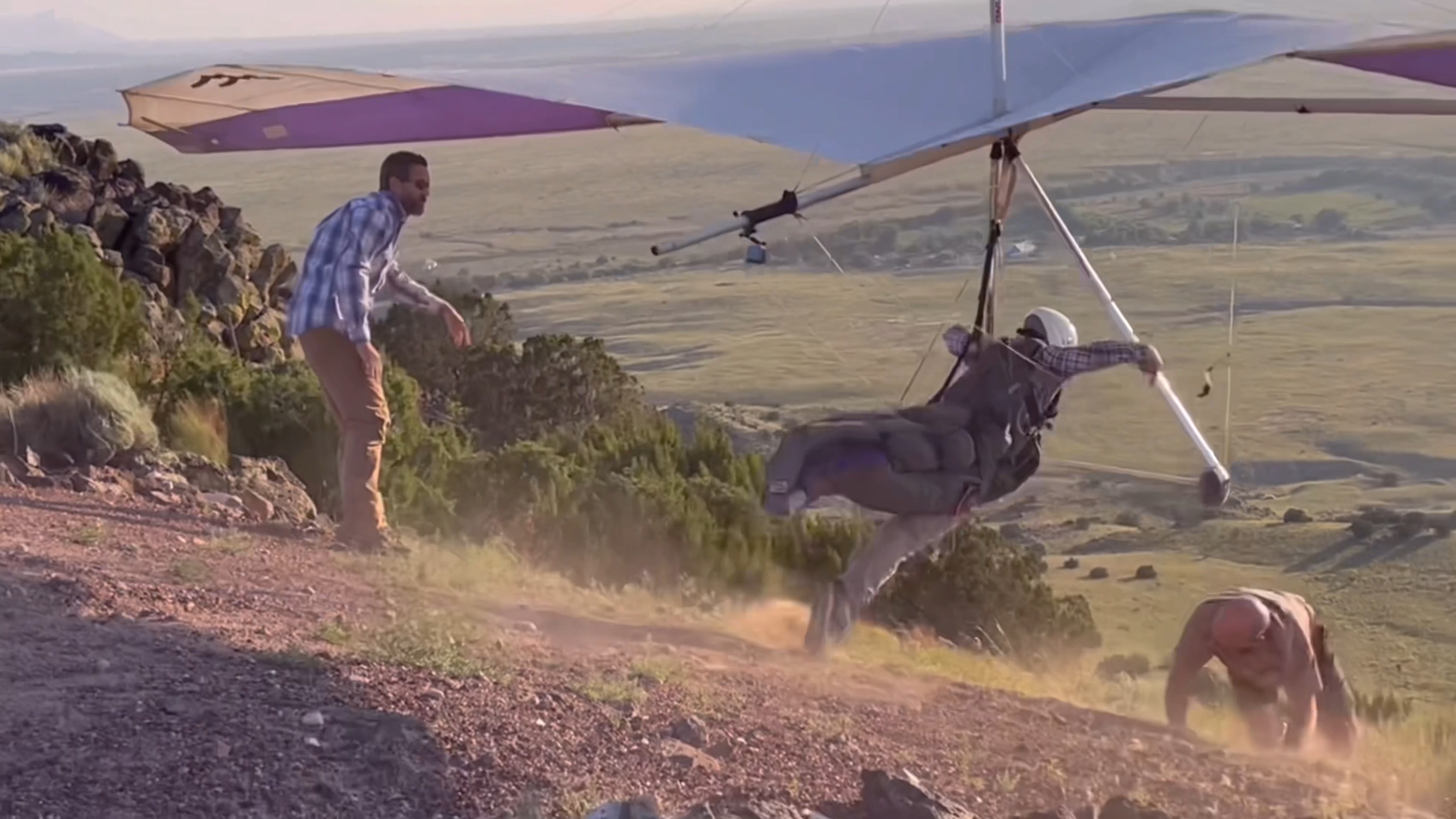 A hang glider pilot launching off a ridge in New Mexico while ground crew help steady the wing.