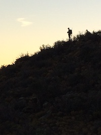 A silhouette of a person carrying gear along a ridge at sunset.